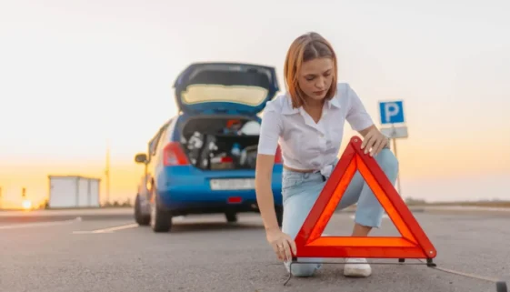 Žena staví za auto výstražný trojúhelník