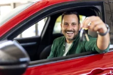 Muž sedí v novém autě a ukazuje klíčky