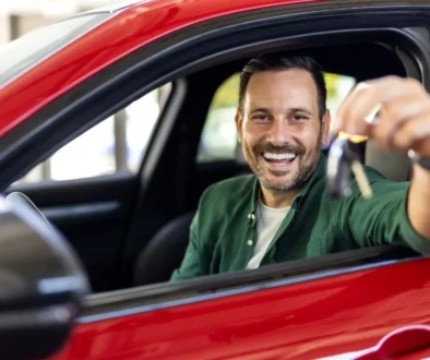 Muž sedí v novém autě a ukazuje klíčky