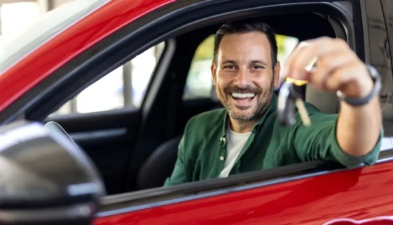 Muž sedí v novém autě a ukazuje klíčky