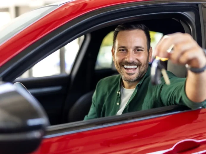 Muž sedí v novém autě a ukazuje klíčky