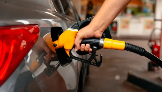 Detailní záběr ruky tankující palivo žlutou pistolí do nádrže osobního automobilu na čerpací stanici.