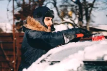 řidič připravuje auto na cestu ometáním sněhu z kapoty a střechy.