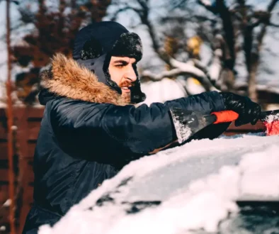 řidič připravuje auto na cestu ometáním sněhu z kapoty a střechy.