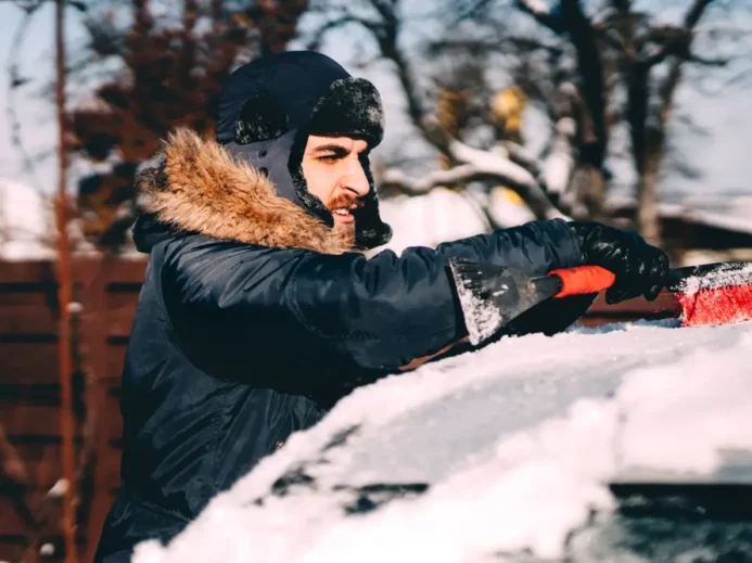 řidič připravuje auto na cestu ometáním sněhu z kapoty a střechy.