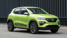 Bright lime-green compact SUV photographed from the front-left, parked on a paved surface with a dark industrial fence behind it.
