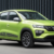 Bright lime-green compact SUV photographed from the front-left, parked on a paved surface with a dark industrial fence behind it.