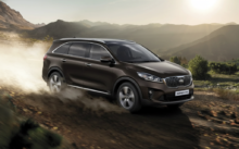 Brown Kia Sorento driving on a dusty mountain dirt road at sunset, kicking up dust behind it.