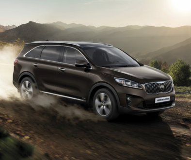 Brown Kia Sorento driving on a dusty mountain dirt road at sunset, kicking up dust behind it.