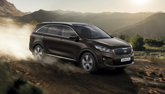 Brown Kia Sorento driving on a dusty mountain dirt road at sunset, kicking up dust behind it.