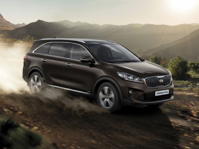 Brown Kia Sorento driving on a dusty mountain dirt road at sunset, kicking up dust behind it.